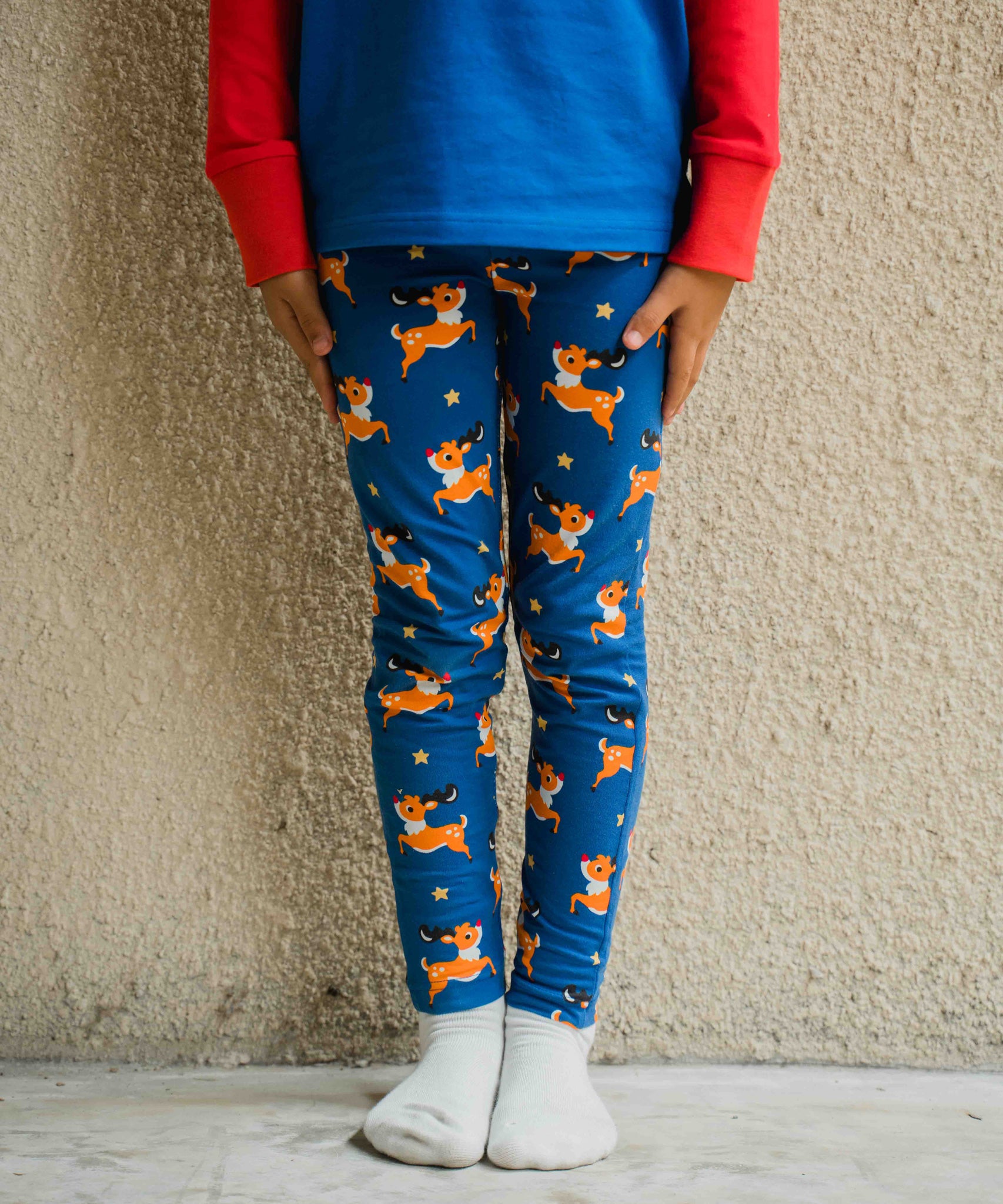 AS close up of a child wearing the Maxomorra Reindeer Leggings. The child is stood in front of a beige coloured wall. 