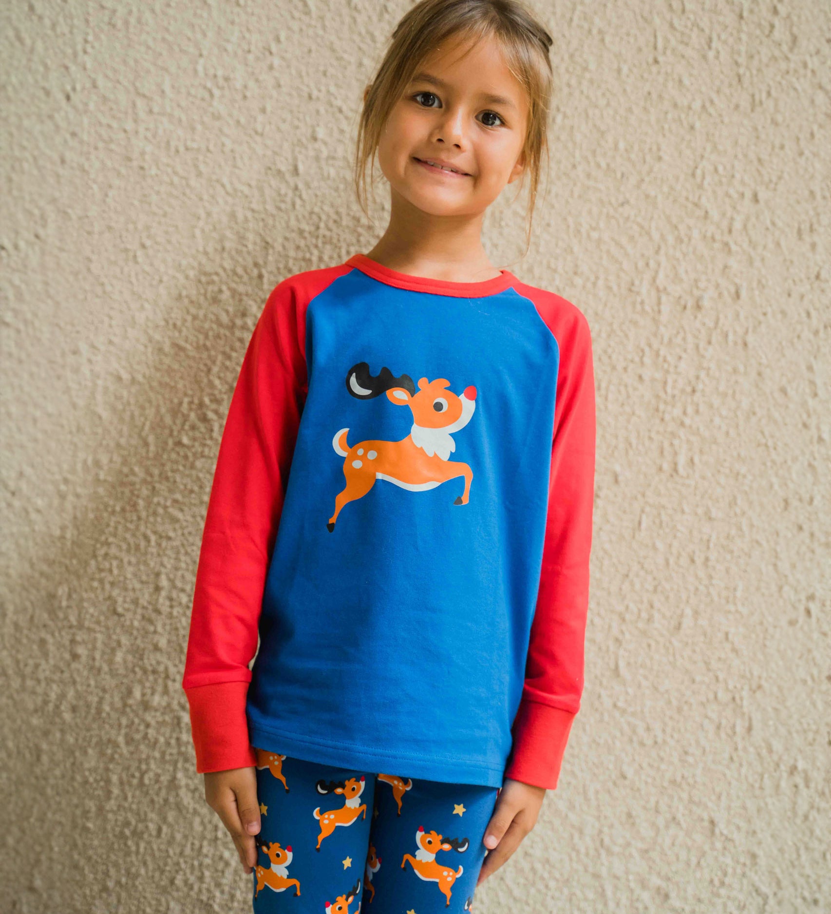 A child wearing a Maxomorra Reindeer Raglan Long Sleeve Top. The child is standing in front of a beige wall. 