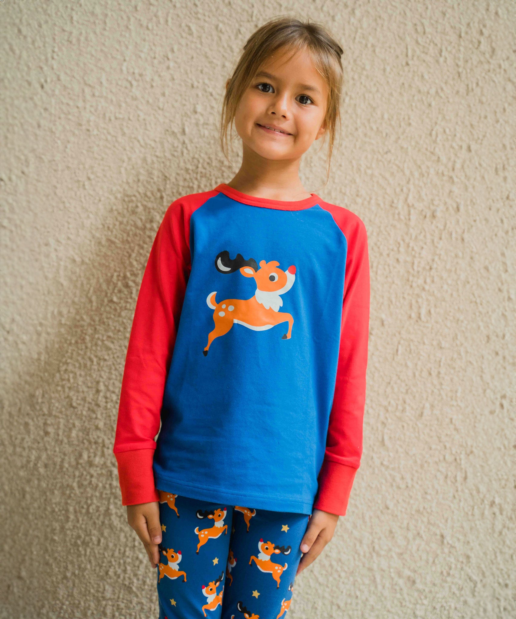 A child wearing a Maxomorra Reindeer Raglan Long Sleeve Top. The child is standing in front of a beige wall. 