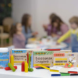 A display of the Medenka beeswax crayon and modelling clay range, with children colouring in the background. 