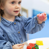  A little girl playing with some pink Medenka beeswax modelling clay. 