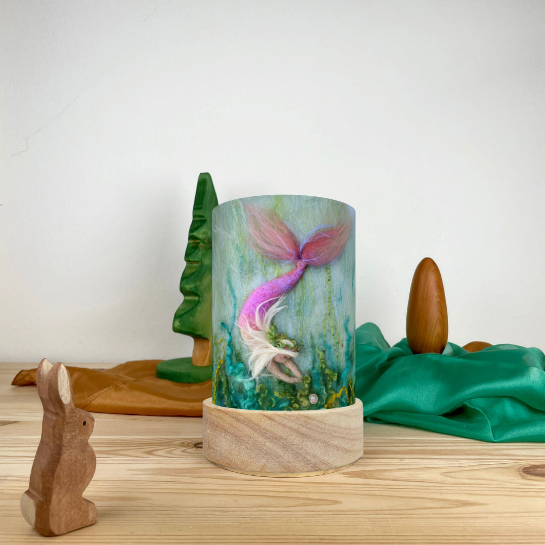 Toverlux Light Wishes Base and Silhouette in Mermaid. A beautiful felt illustration on a mermaid finding a pearl. The Light Wish is set on a wooden table with a wooden rabbit in front