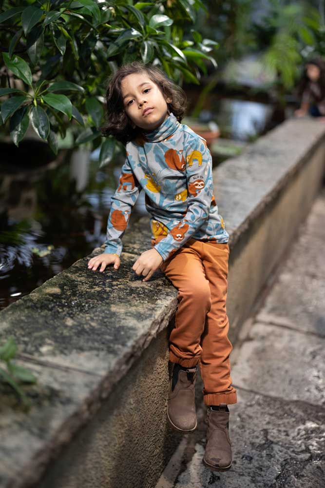 Young boy sat on a wall in front of a tree wearing the Meyadey turtle neck sloth print top