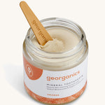 An opened jar of the Georganics orange mineral toothpaste with the tongue stick dipped in