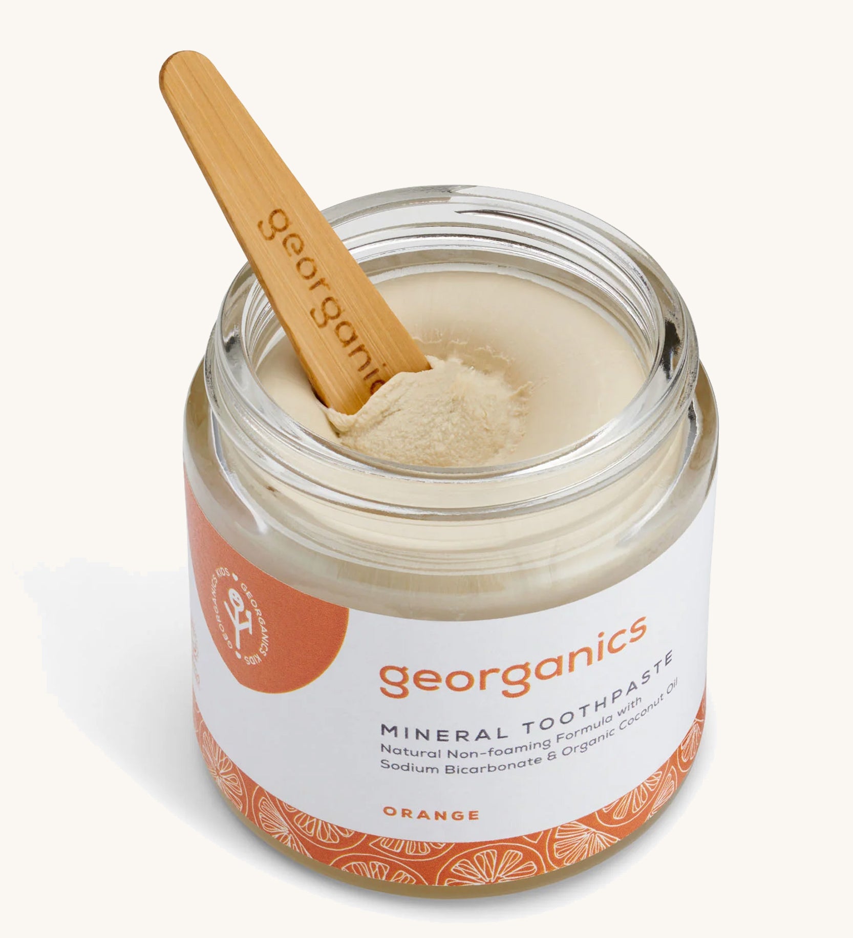 An opened jar of the Georganics orange mineral toothpaste with the tongue stick dipped in