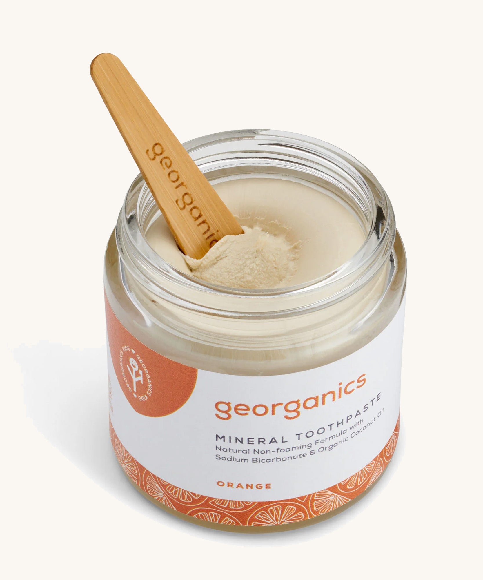 An opened jar of the Georganics orange mineral toothpaste with the tongue stick dipped in