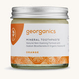 A jar of the Georganics orange mineral toothpaste on a cream background