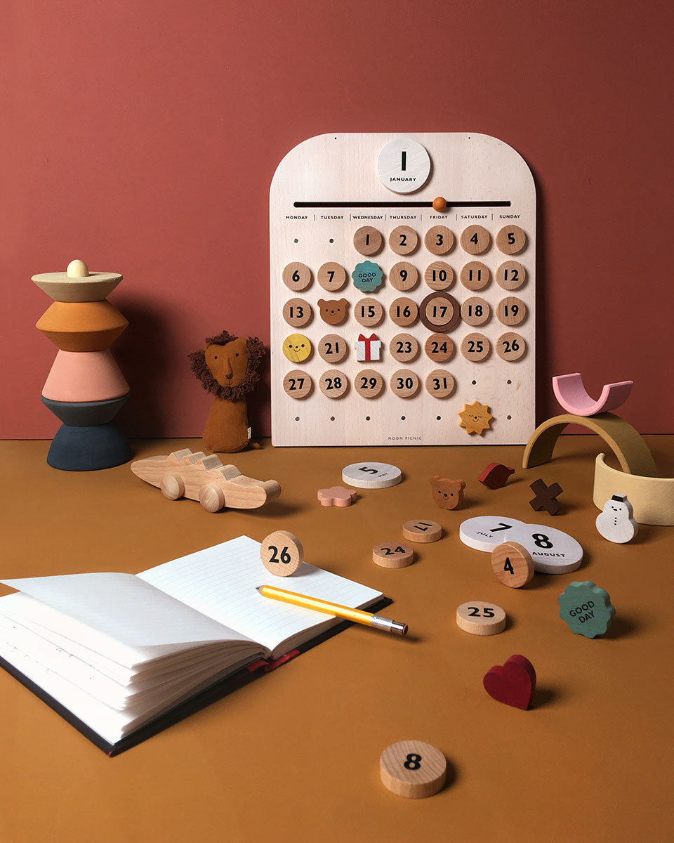 Pieces of the Moon Picnic wooden calendar scattered on a brown table in front of a red wall