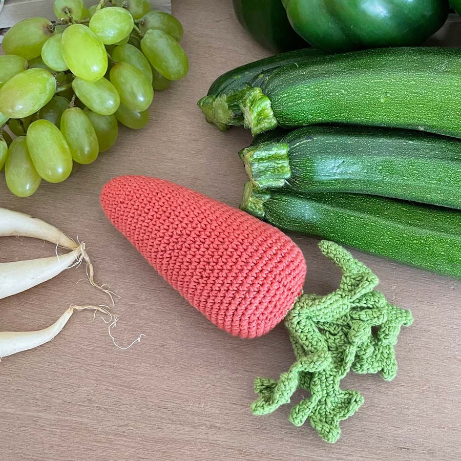 Myum handmade soft crochet carrot toy on a wooden table next to come real vegetables