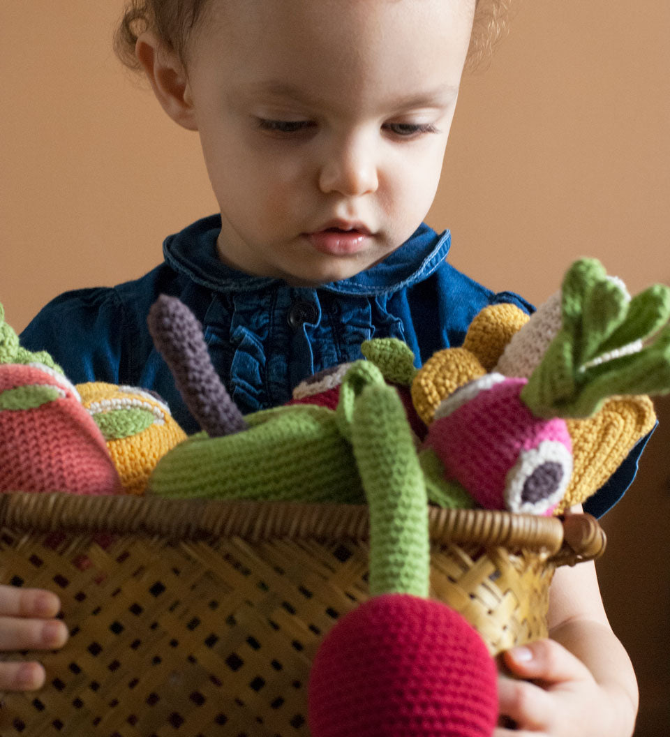 Girl holding a basket full of Myum handmade crochet soft vegetable toys in front of a beige wall