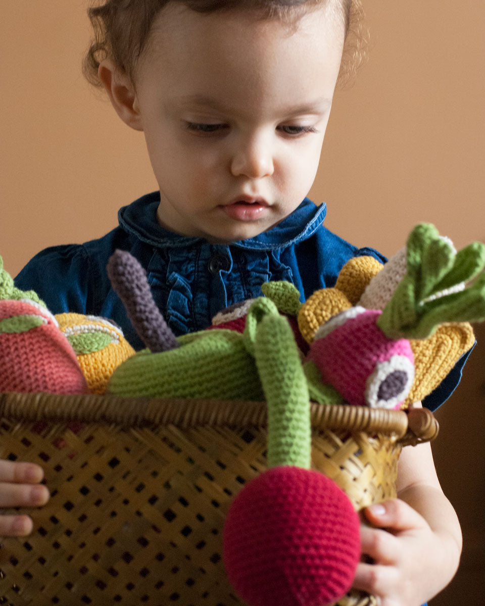 Girl holding a basket full of Myum handmade crochet soft vegetable toys in front of a beige wall