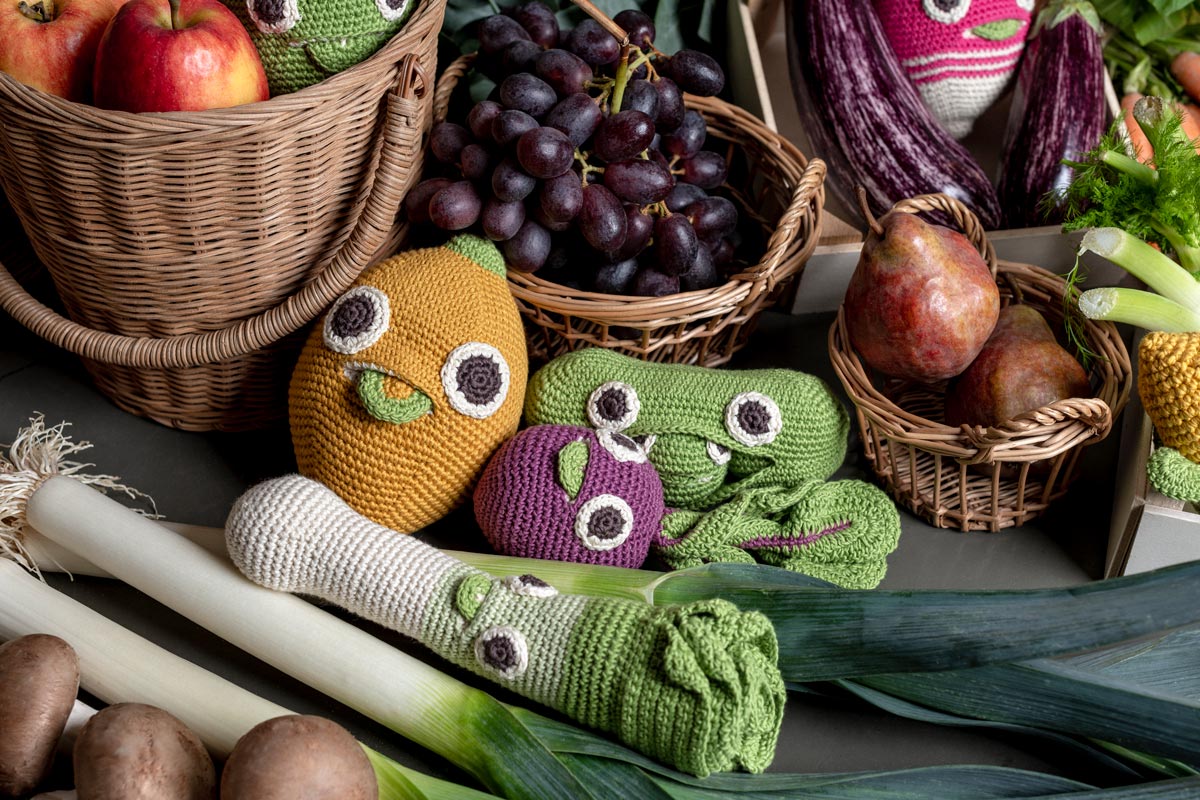 Myum handmade organic cotton soft crochet vegetable toys laid out on a table around real fruit and vegetables