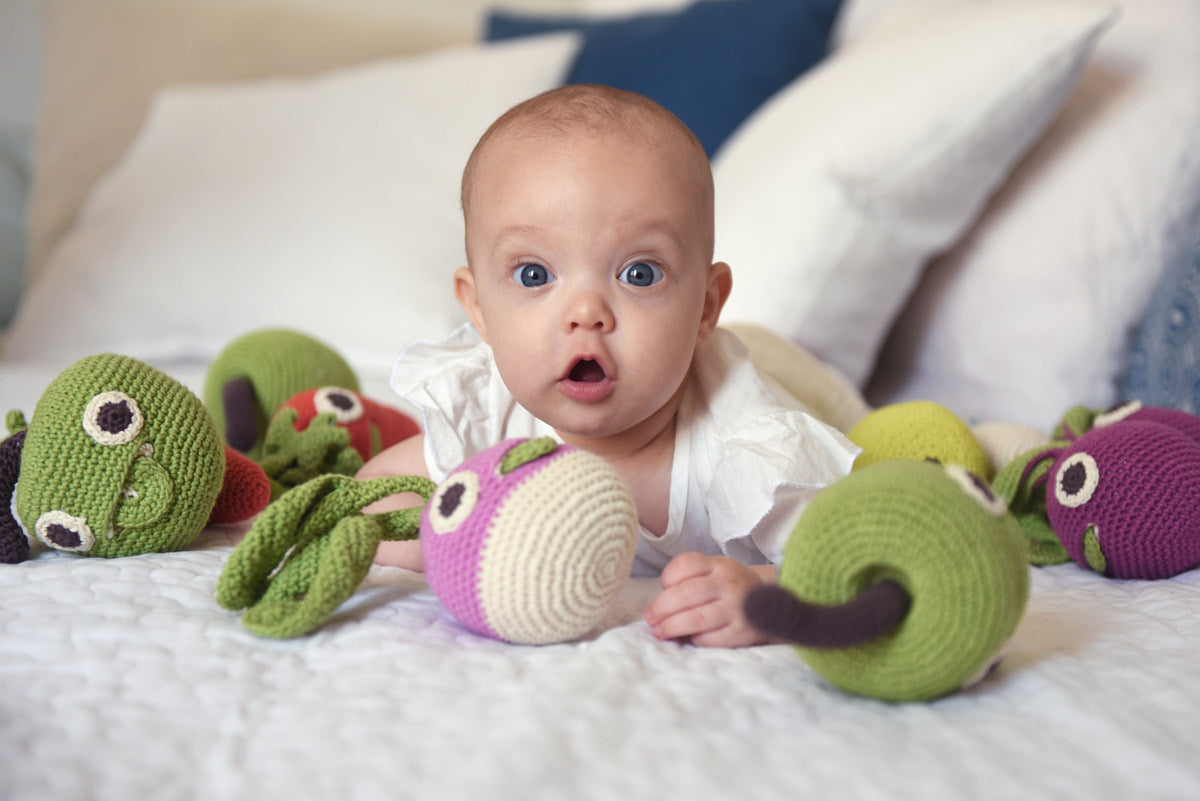 Baby laying on a bed next to some Myum eco-friendly plastic free soft crochet vegetable toys