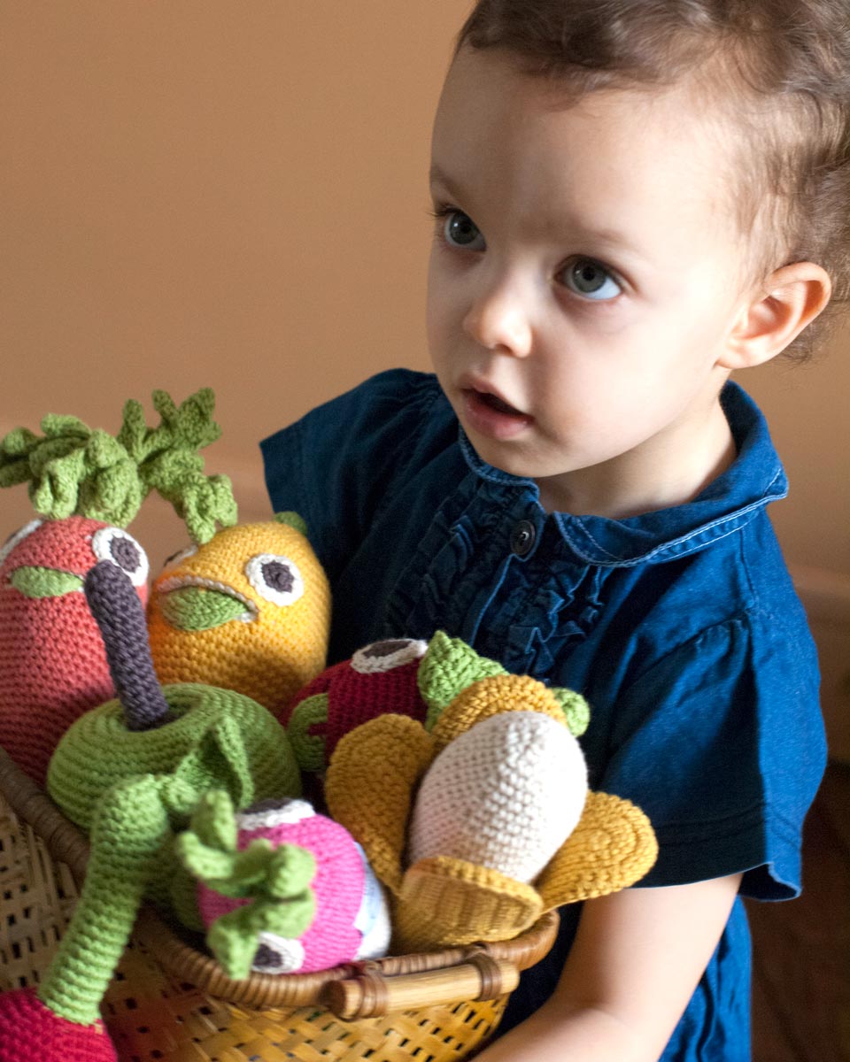 Girl holding a wooden basket full of Myum eco-friendly crochet soft toys on a beige background