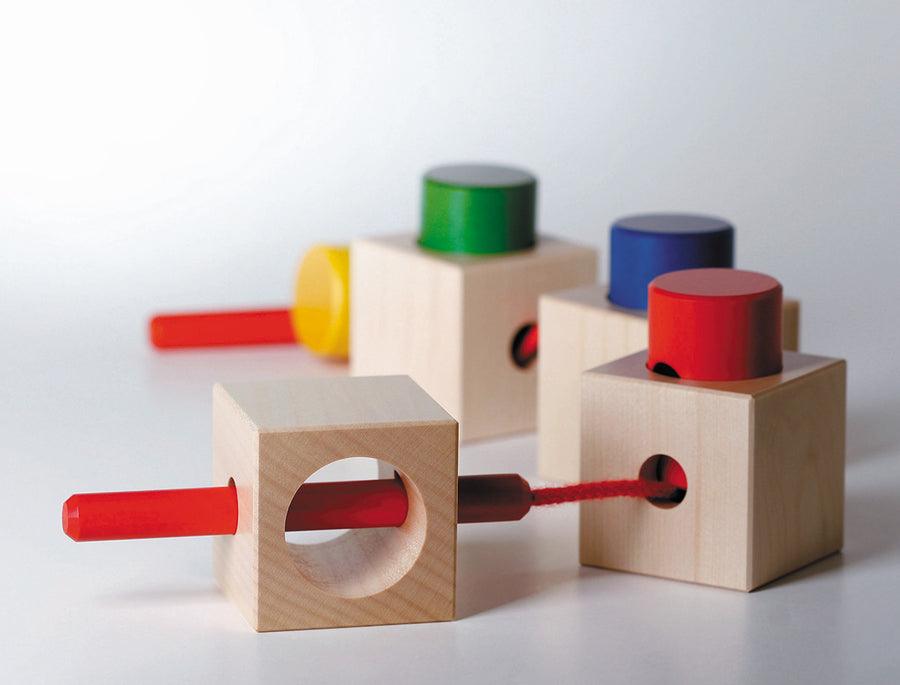 Naef Signa wooden threading toy assembled in a train on a white background. Shows 4 wooden cubes and 4 wooden cylinders with thread weaving through holes in a long curving line.