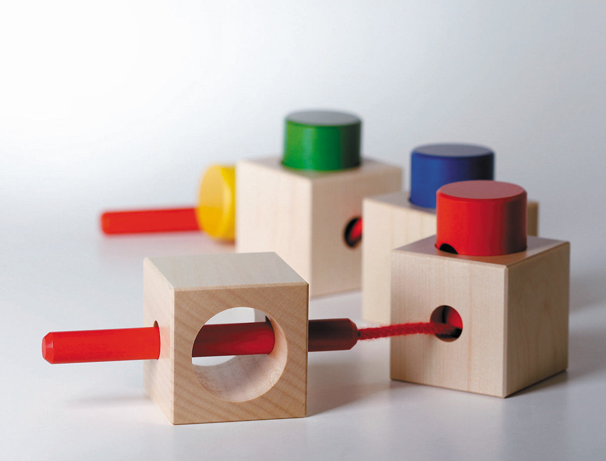 Naef Signa wooden threading toy assembled in a train on a white background. Shows 4 wooden cubes and 4 wooden cylinders with thread weaving through holes in a long curving line.