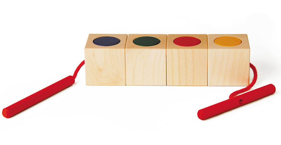 Naef Signa wooden threading toy lined up in a line on a white background. Shows 4 wooden cubes in a line with cylcinders slotted into holes within the cubes. The thread is shown running through all the wooden pieces.