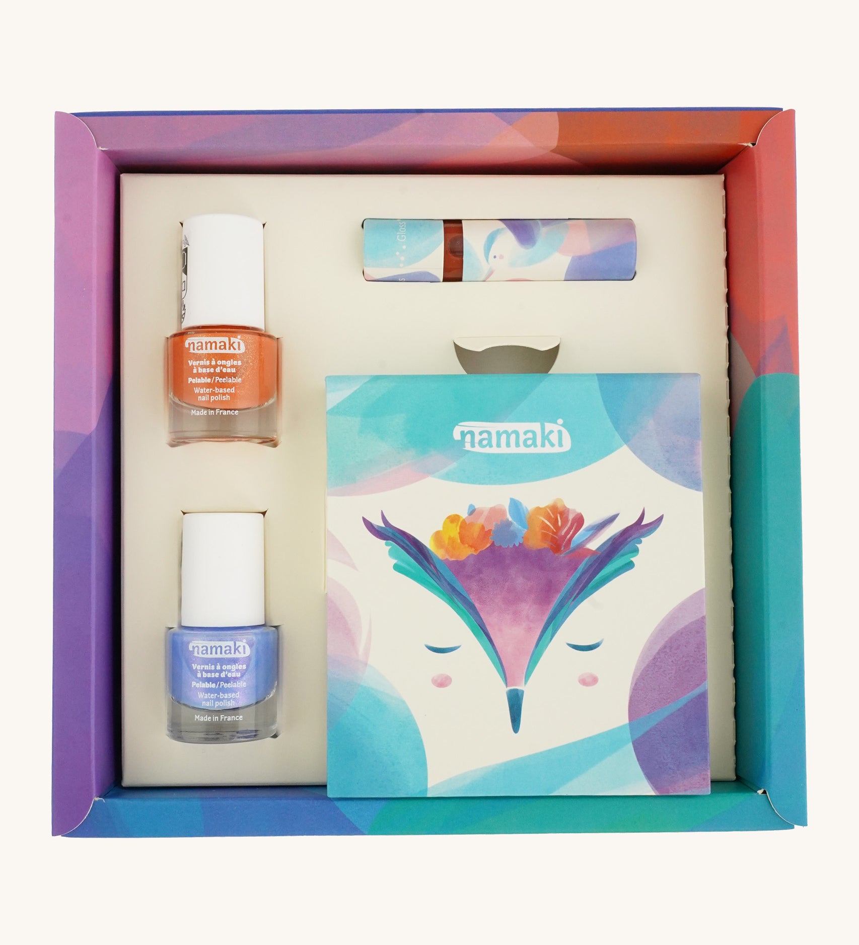 An open cardboard box for the Namaki fairy moonlight make up set which includes a blue and orange nail polish, a eye shadow set and a lipgloss on a cream background.