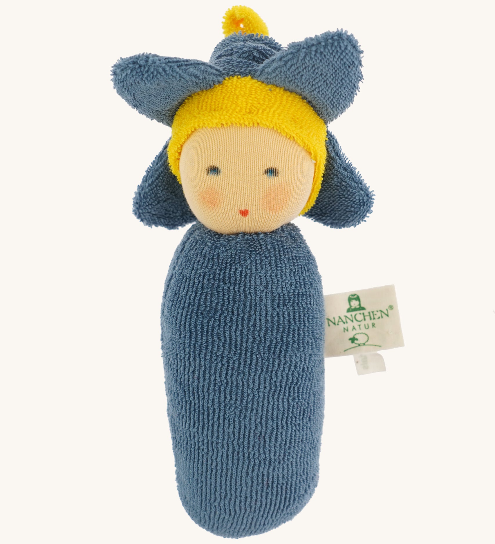 Nanchen Flower Rattle Doll - Forget-Me-Not, is a soft, organic and handmade sensory doll toy with a blue body, a little blue hat with blue forget-me-not leaves and a yellow strip of fabric to mimic hair. This doll also has an adorable face with blue eyes