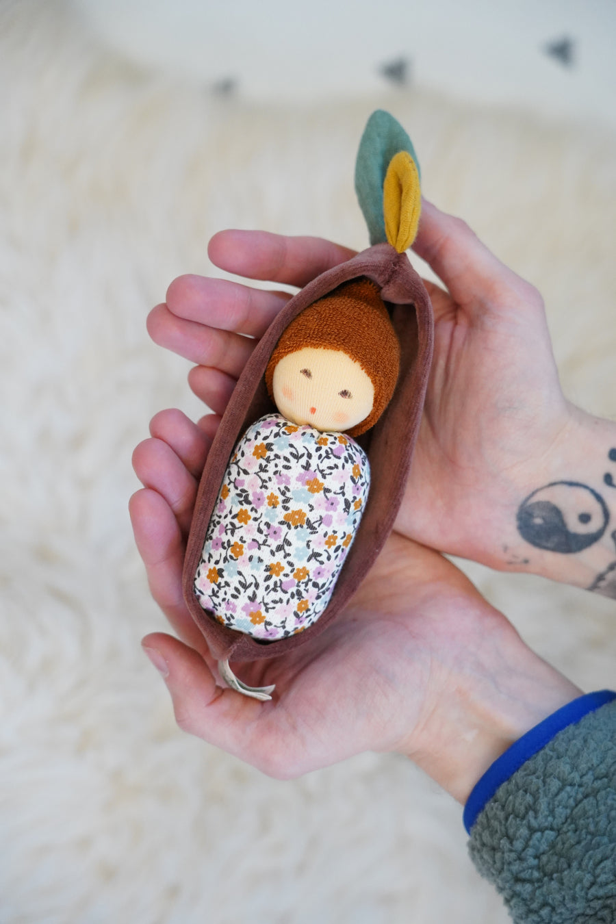 Nanchen Oak Baby Waldorf Doll - Floral. A little organic grasping doll in a brown velvet cradle in a persons hands.