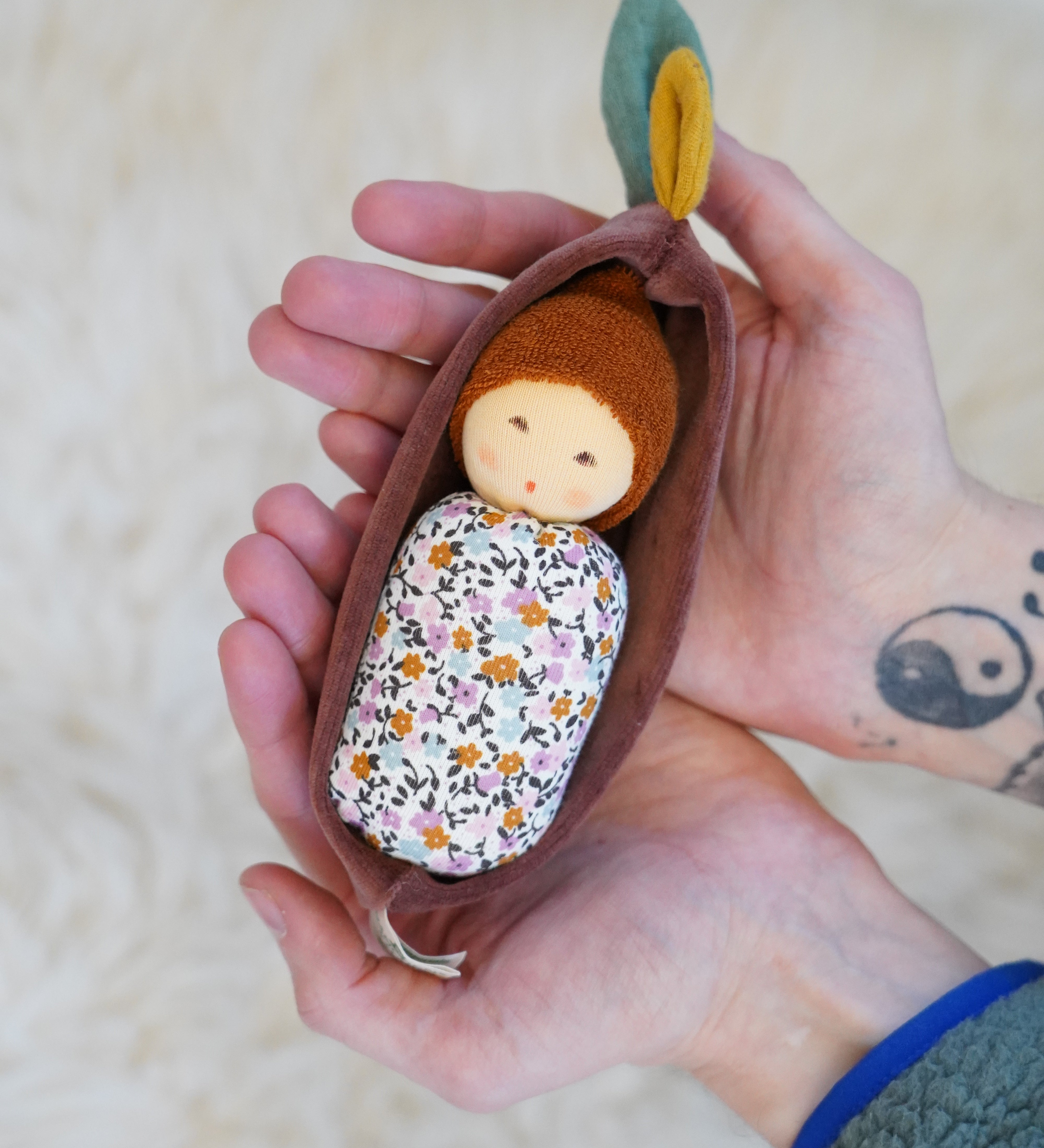 Nanchen Oak Baby Waldorf Doll - Floral. A little organic grasping doll in a brown velvet cradle in a persons hands.