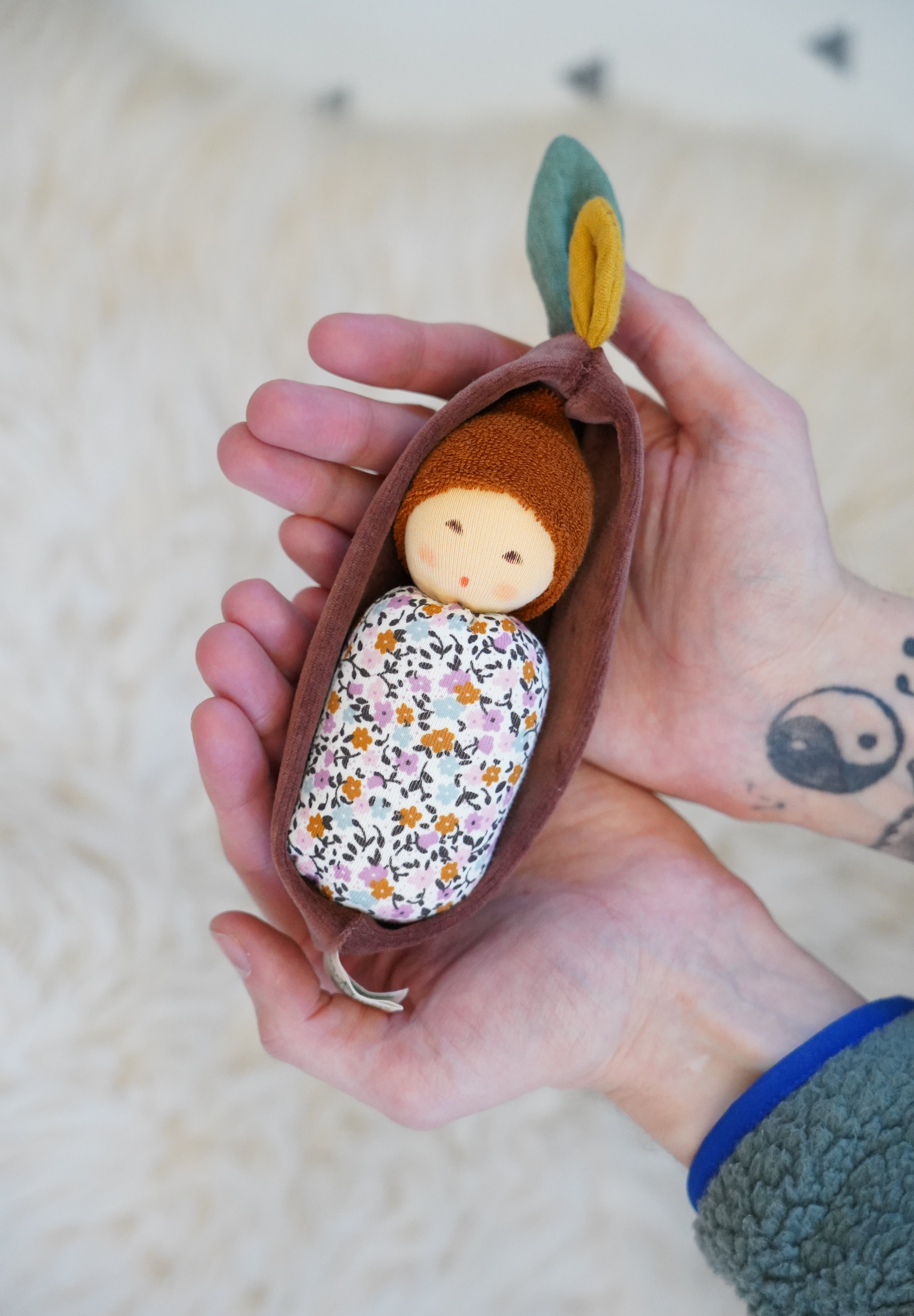 Nanchen Oak Baby Waldorf Doll - Floral. A little organic grasping doll in a brown velvet cradle in a persons hands.