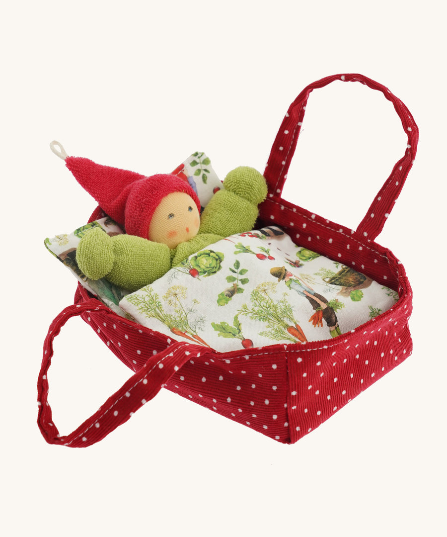 A Nanchen red with white dots carry cot for a Nanchen doll tucked in a garden blanket on a cream background.