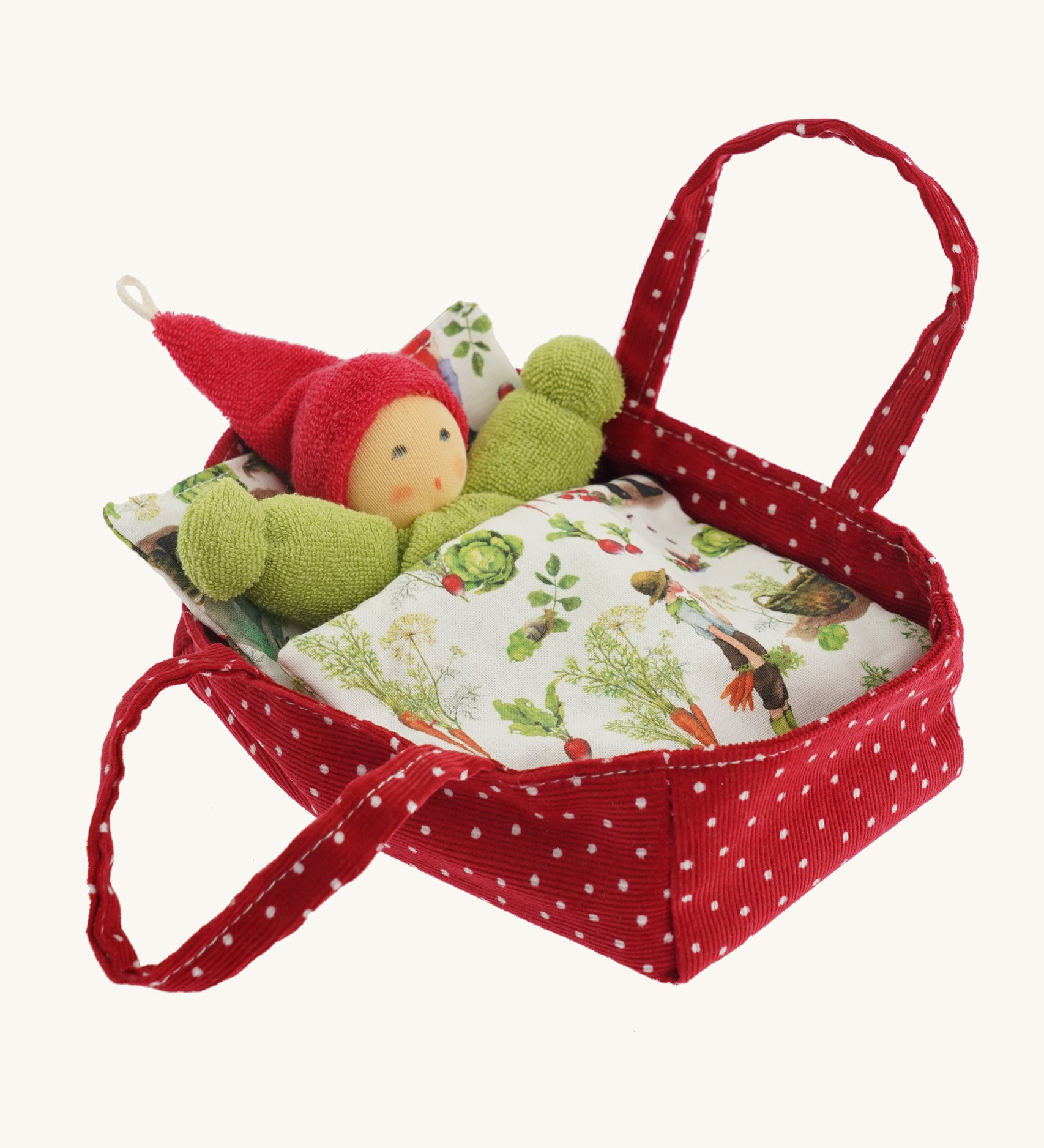 A Nanchen red with white dots carry cot for a Nanchen doll tucked in a garden blanket on a cream background.