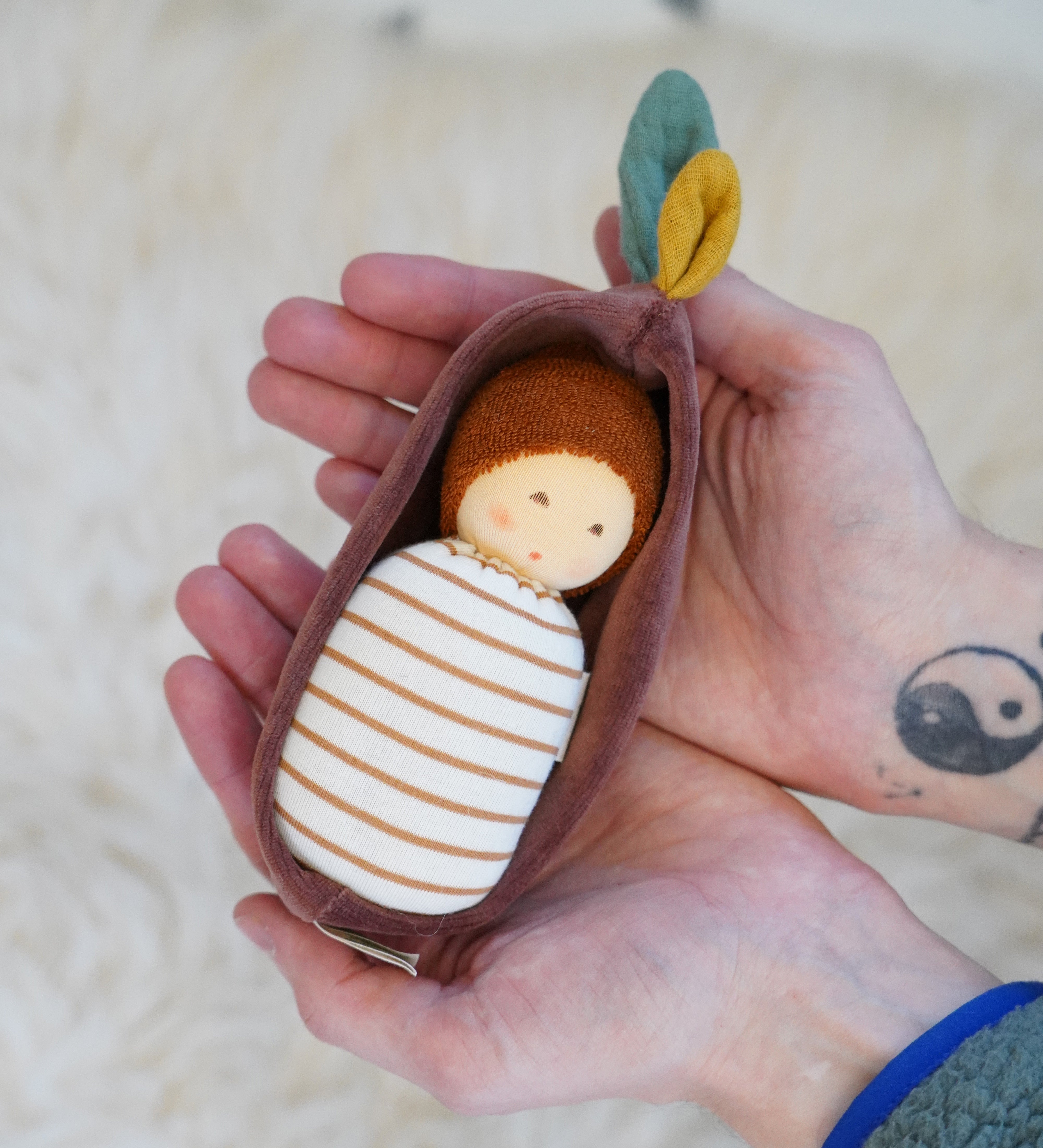 Nanchen Oak Baby Waldorf Doll - Stripes. A little organic grasping doll in a brown velvet cradle in a persons hands.