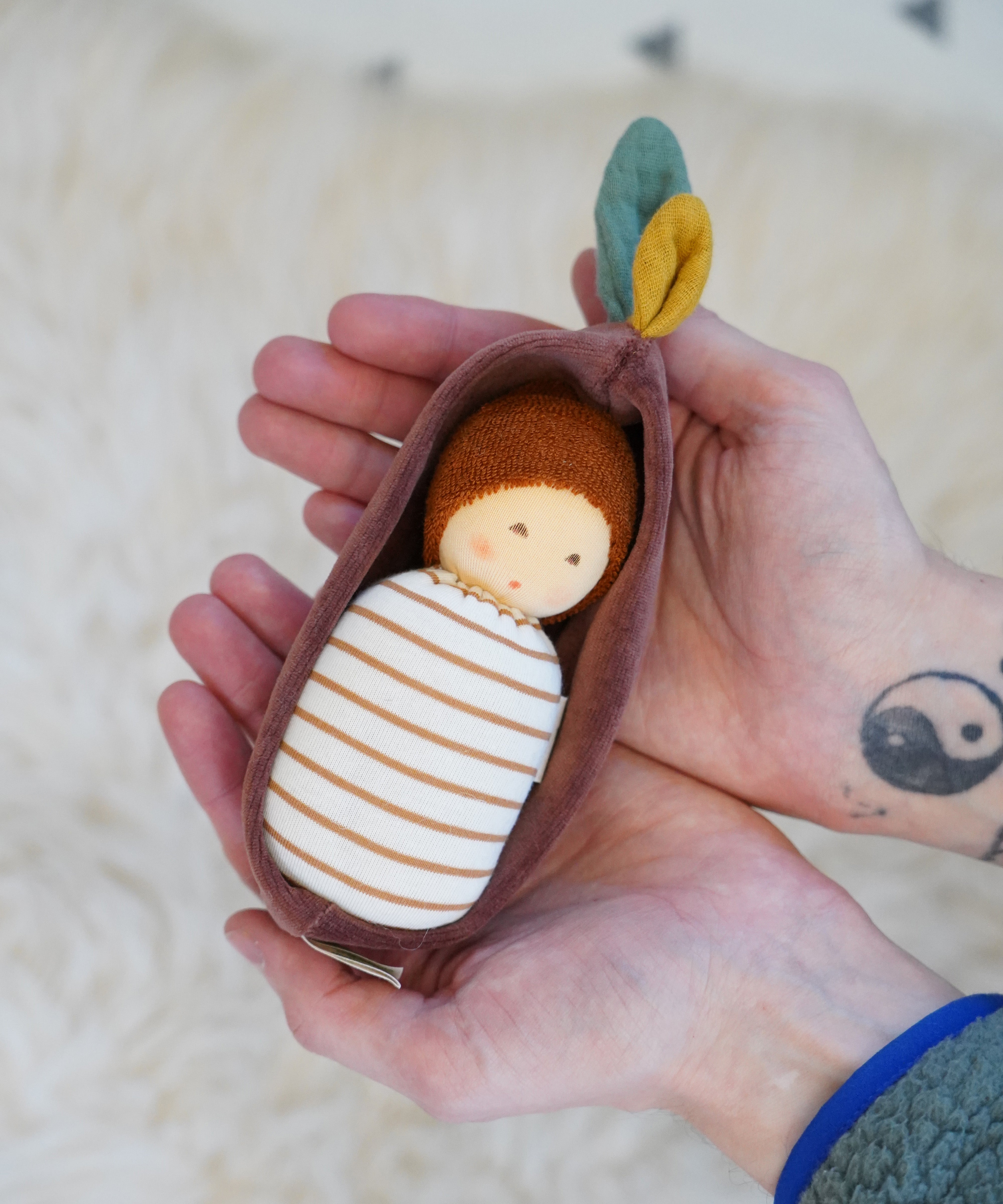 Nanchen Oak Baby Waldorf Doll - Stripes. A little organic grasping doll in a brown velvet cradle in a persons hands.