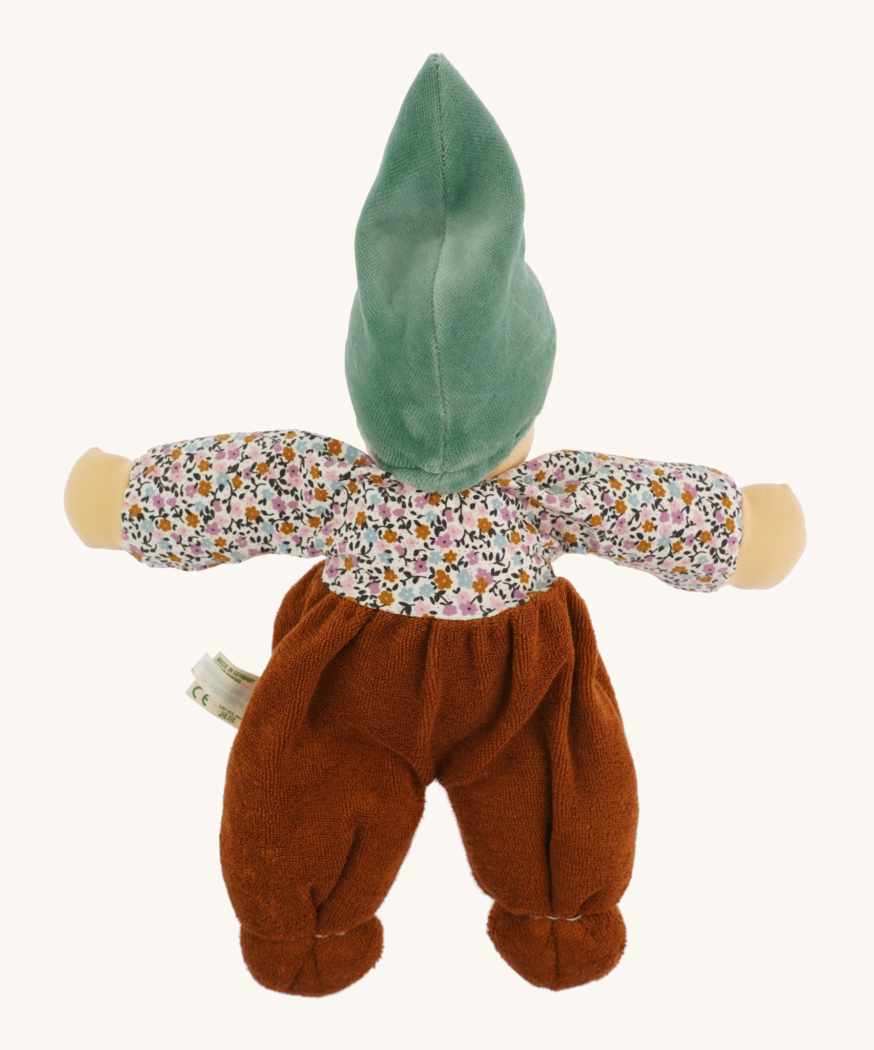 The back of the Nanchen Forest Child Waldorf Doll - Sage. This beautifully handcrafted doll wears sage velour trousers, a brown hat and a floral top. On a cream background