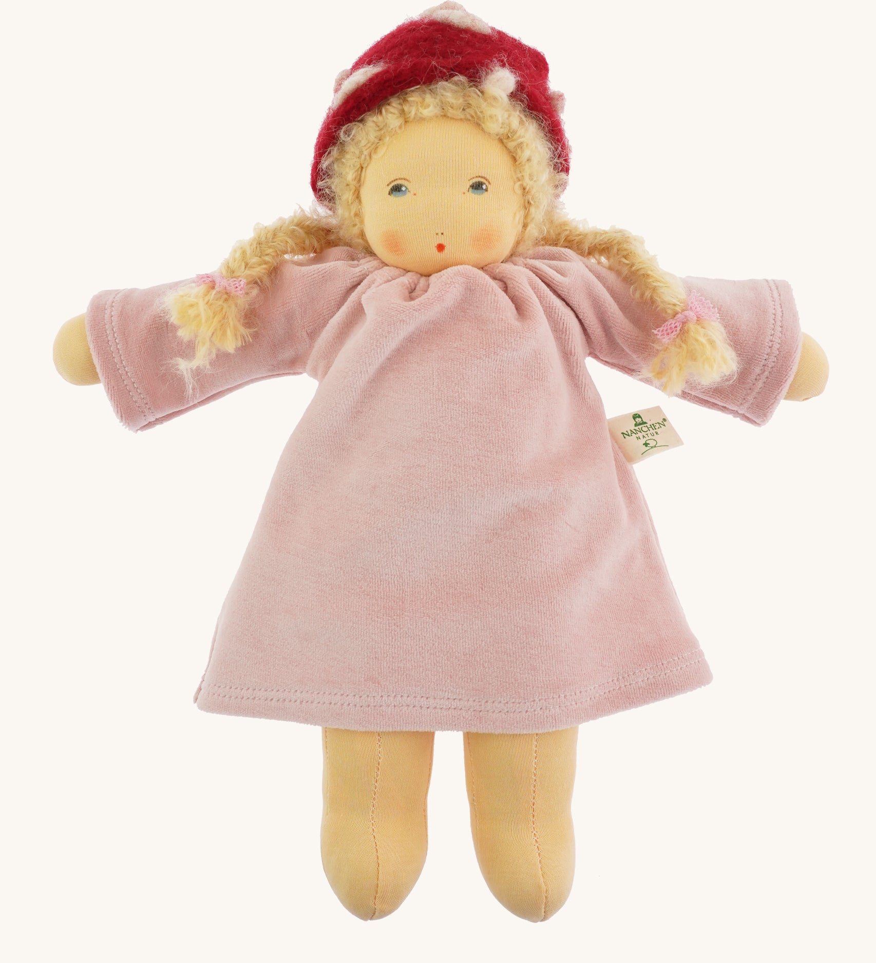 Nanchen Gardenchild Doll, Lolle is a beautiful handcrafted Waldorf doll toy. With a light pink dress, an adorable hand painted face with blue eyes, blonde hair in two braids each secured with red ribbons, and a red and white mushroom style hat. On a cream background