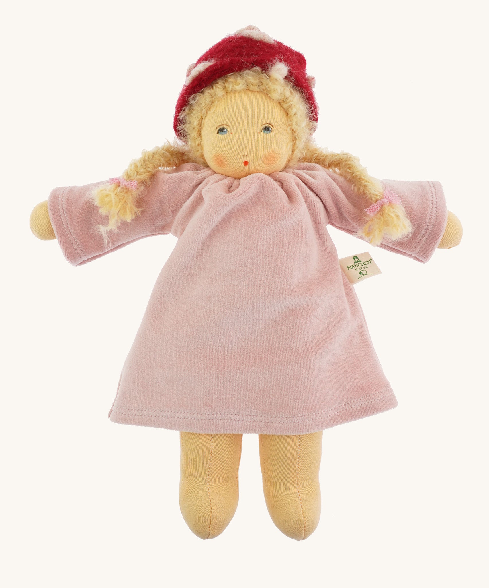 Nanchen Gardenchild Doll, Lolle is a beautiful handcrafted Waldorf doll toy. With a light pink dress, an adorable hand painted face with blue eyes, blonde hair in two braids each secured with red ribbons, and a red and white mushroom style hat. On a cream background