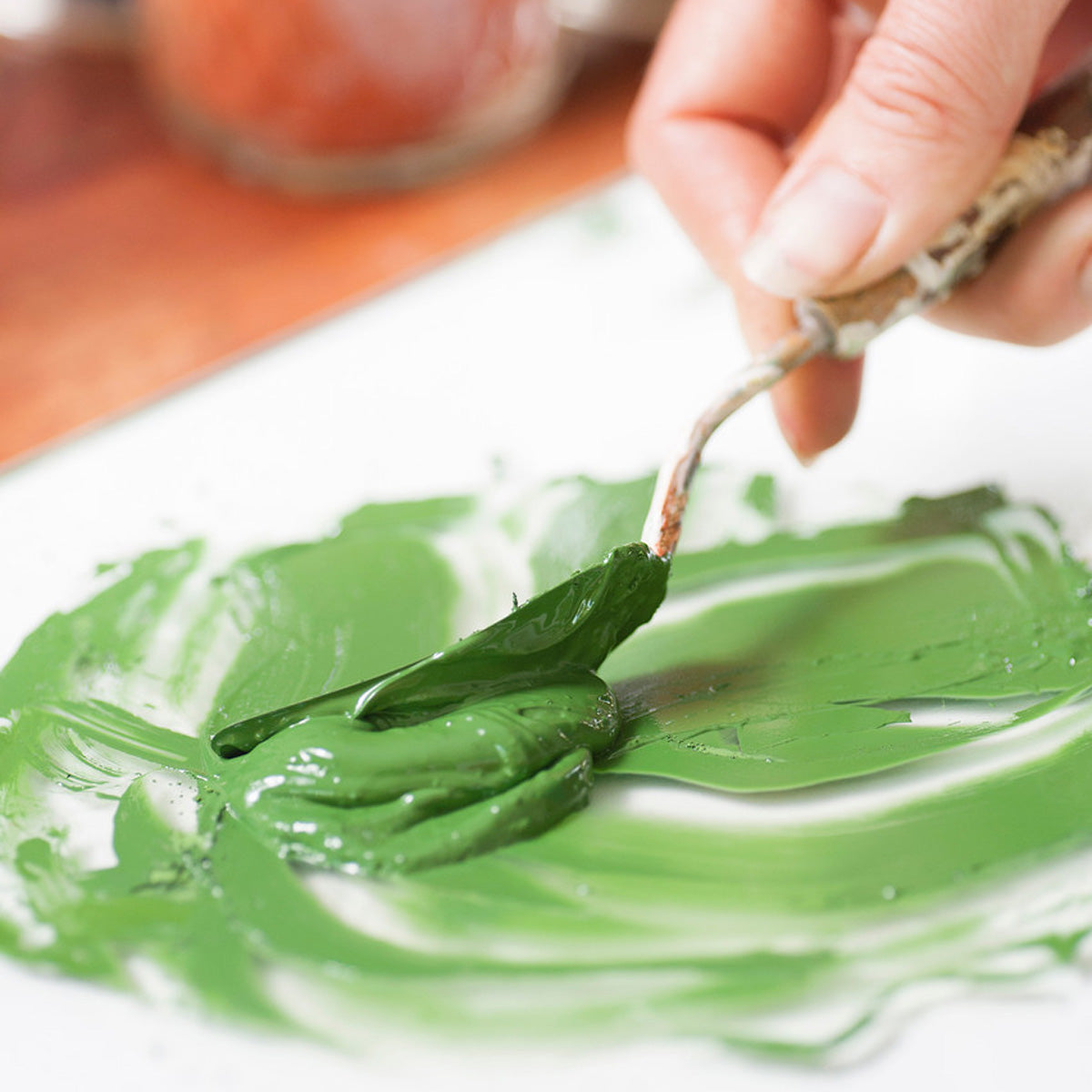 Close up of a hand spreading green Natural Earth oil paint on a white sheet