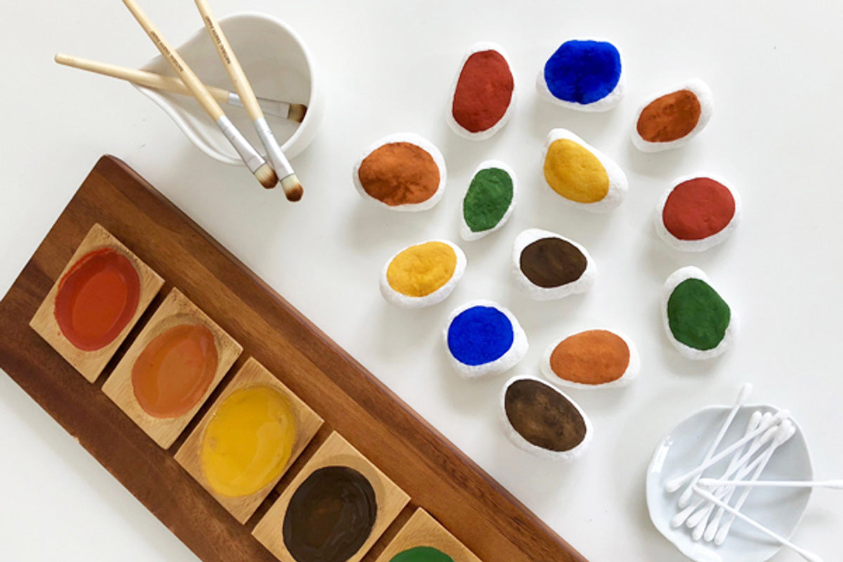 Close up of some pebbles painted in white and coloured Natural Earth eco-friendly paints on a white table