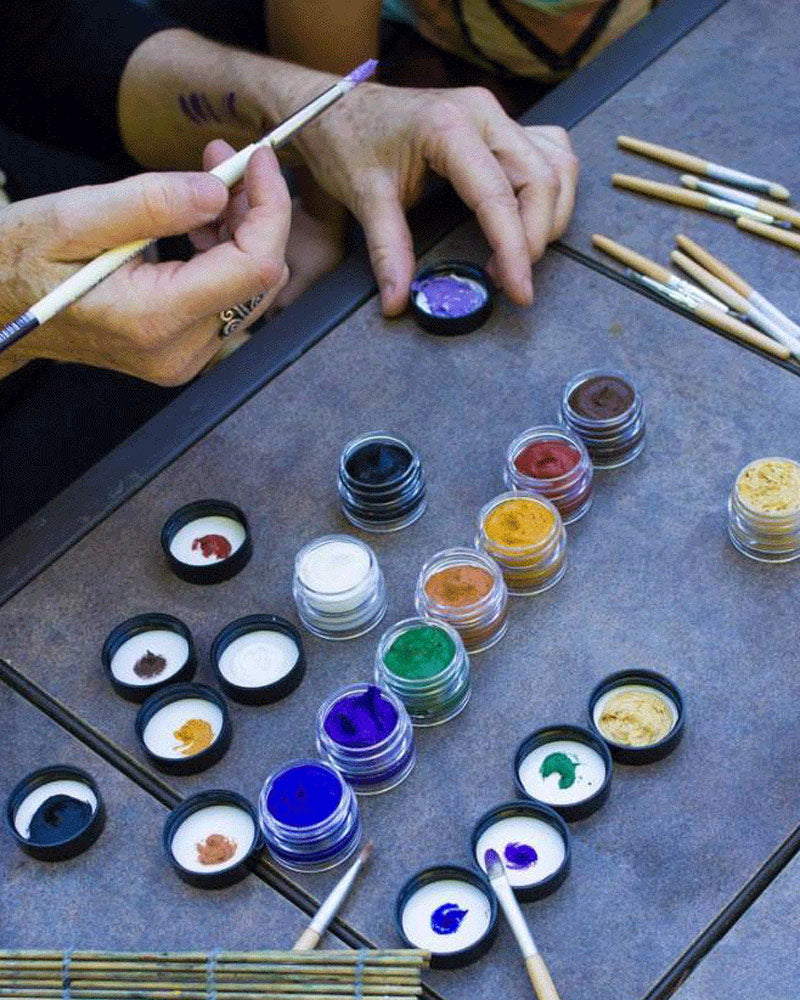 Close up of some hands painting with the Natural Earth kids coloured face paint jars on a grey table