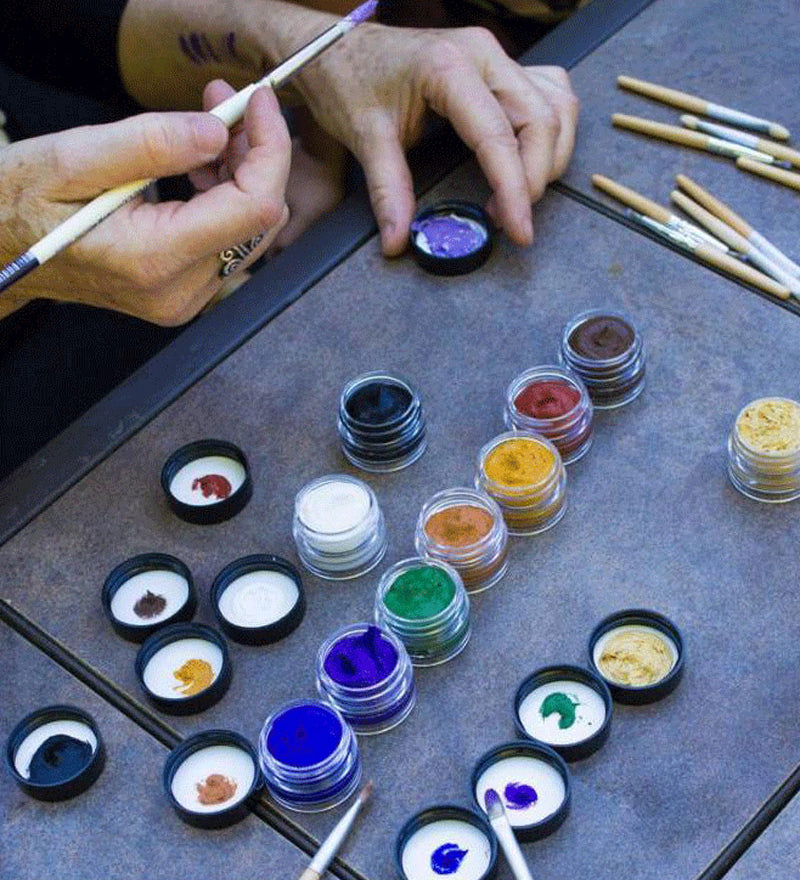 Close up of some hands painting with the Natural Earth kids coloured face paint jars on a grey table