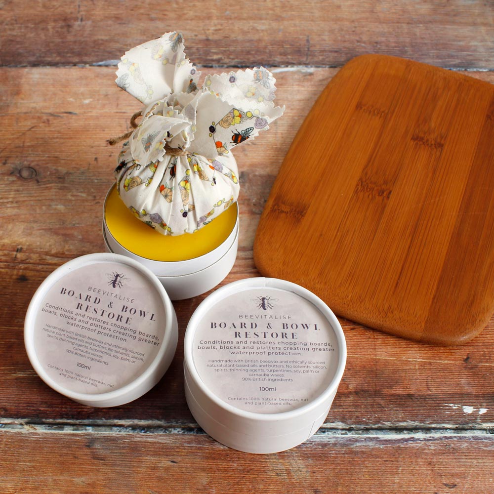 leather revive and board and bowl restore balm on a wooden floor next to a wooden chopping board and leather wallet