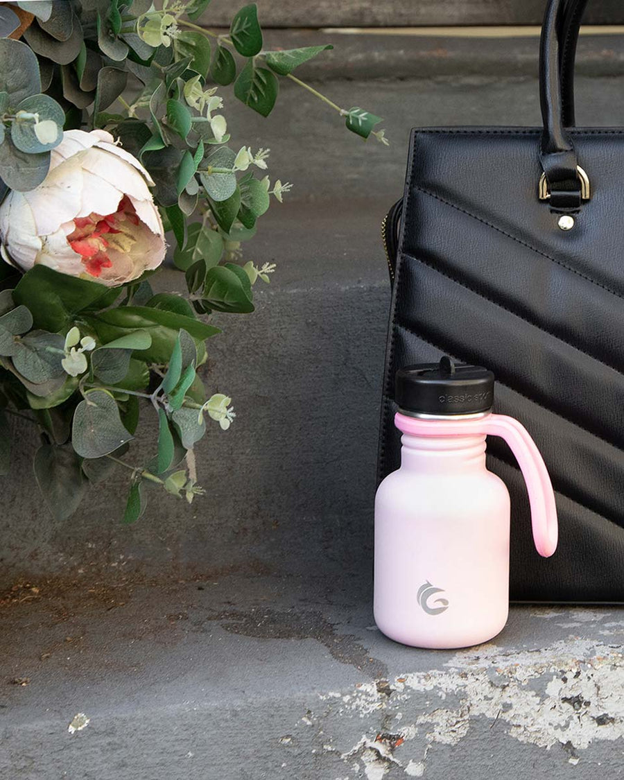 One Green Bottle 350ml plastic free water bottle on a step in front of a black hand bag and next to a white flower