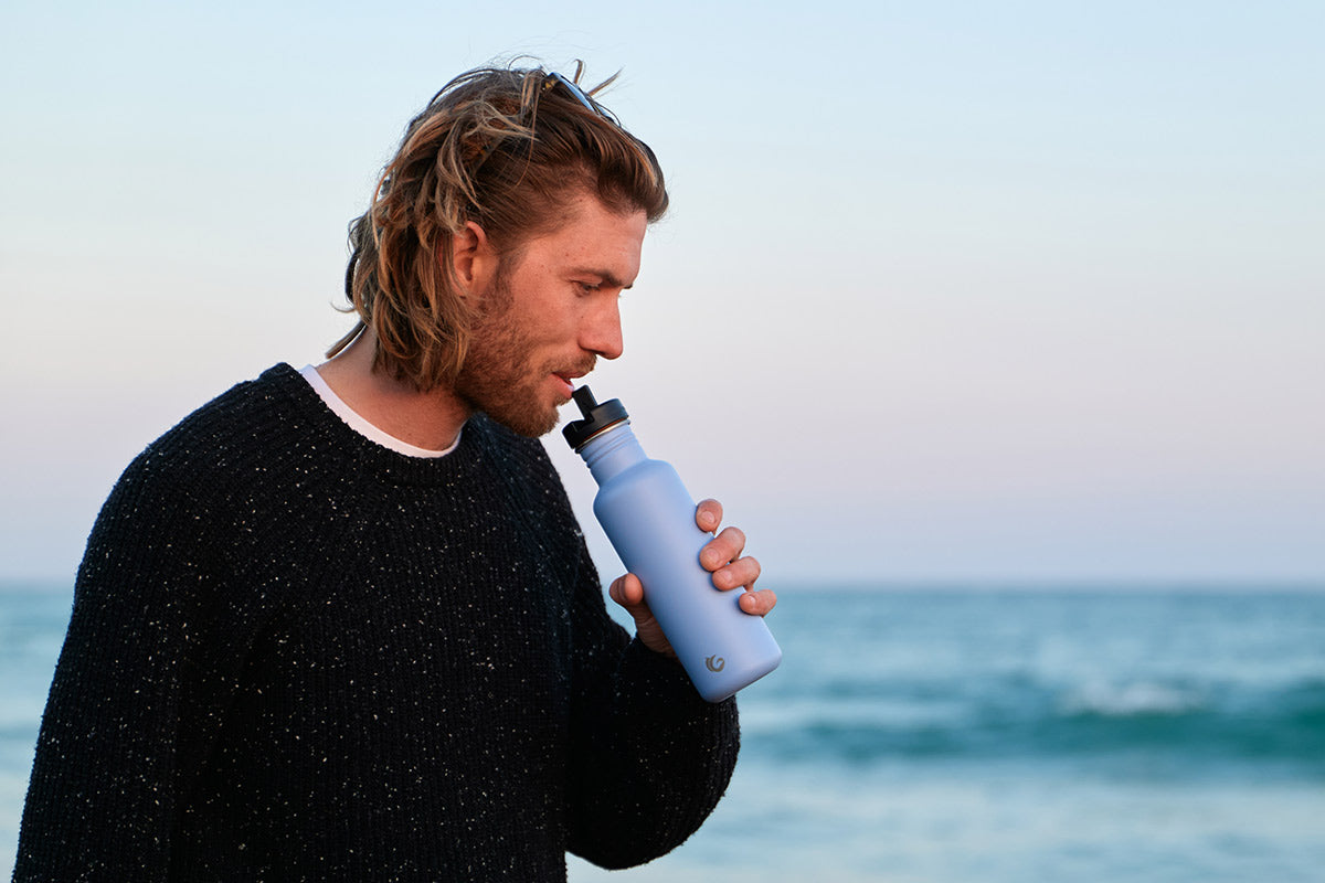 Man drinking from a One Green Bottle eco-friendly metal canteen in front of the sea