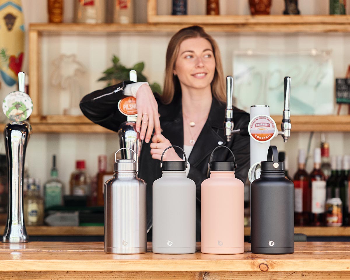 Woman leaning at a bar behind a row of assorted One Green Bottle 2 litre eco-friendly water bottles