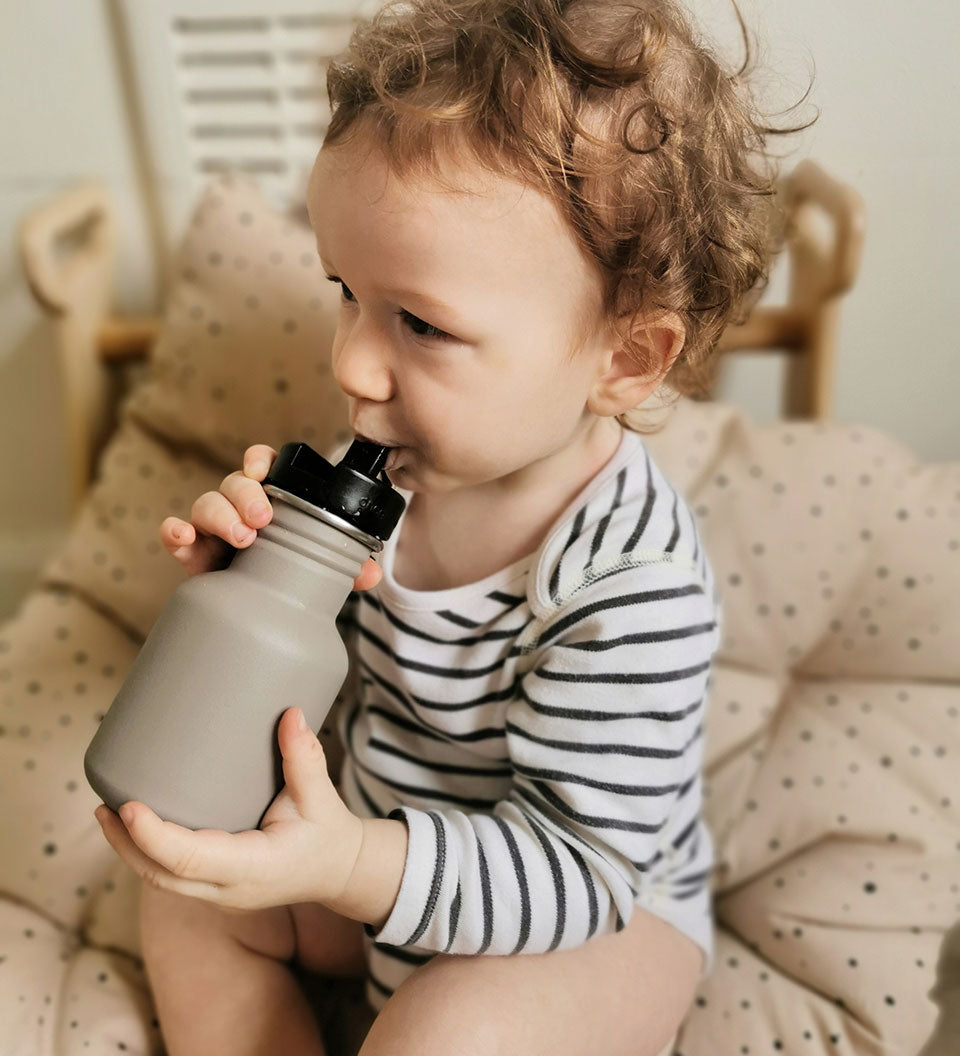 Child holding the One Green Bottle 350ml plastic free tough water bottle sat on a brown cushion