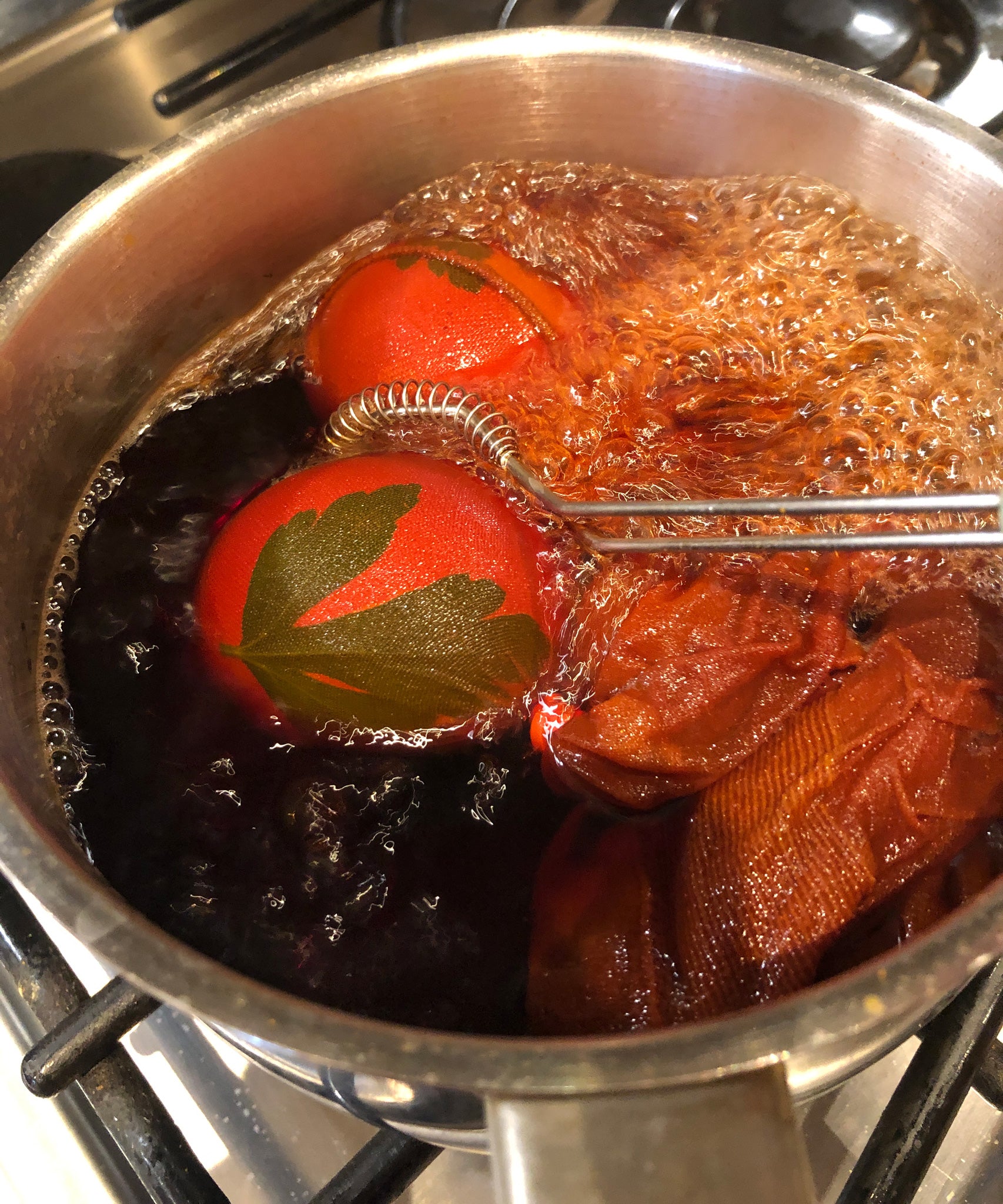 Eggs in a saucepan showing the OkoNorm egg dye kit in use. The egg has started dying in a pink toned colour. 