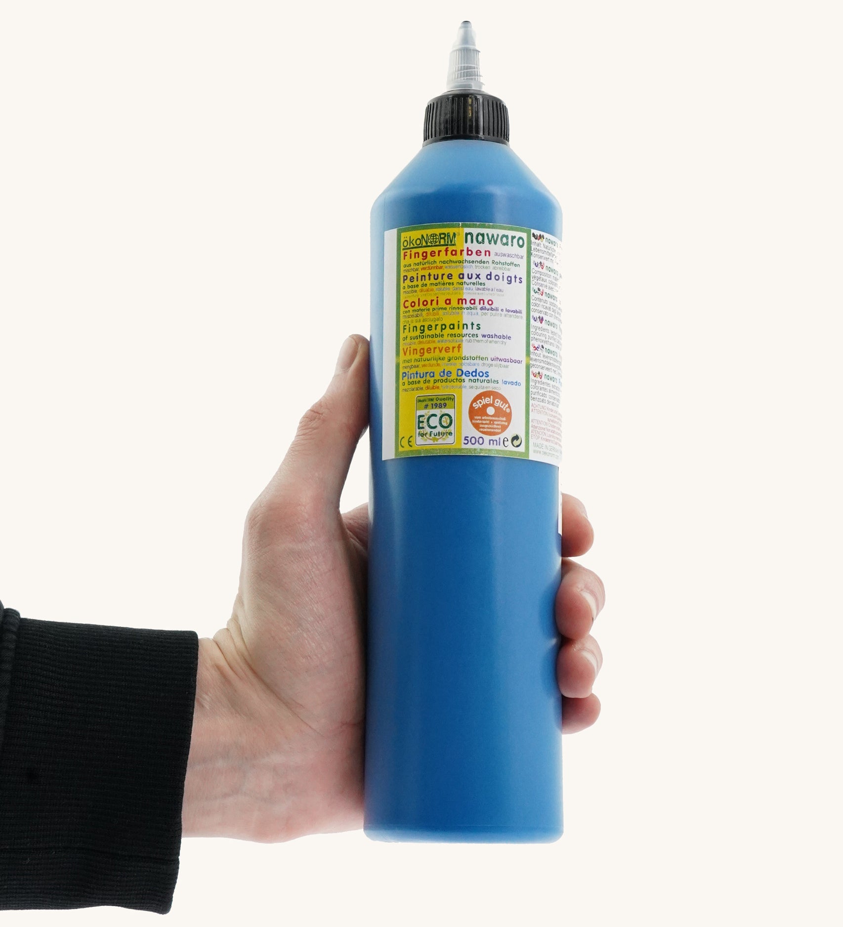 An adult's hand holding a 500ml bottle of OkoNorm finger paints in a blue colour. 