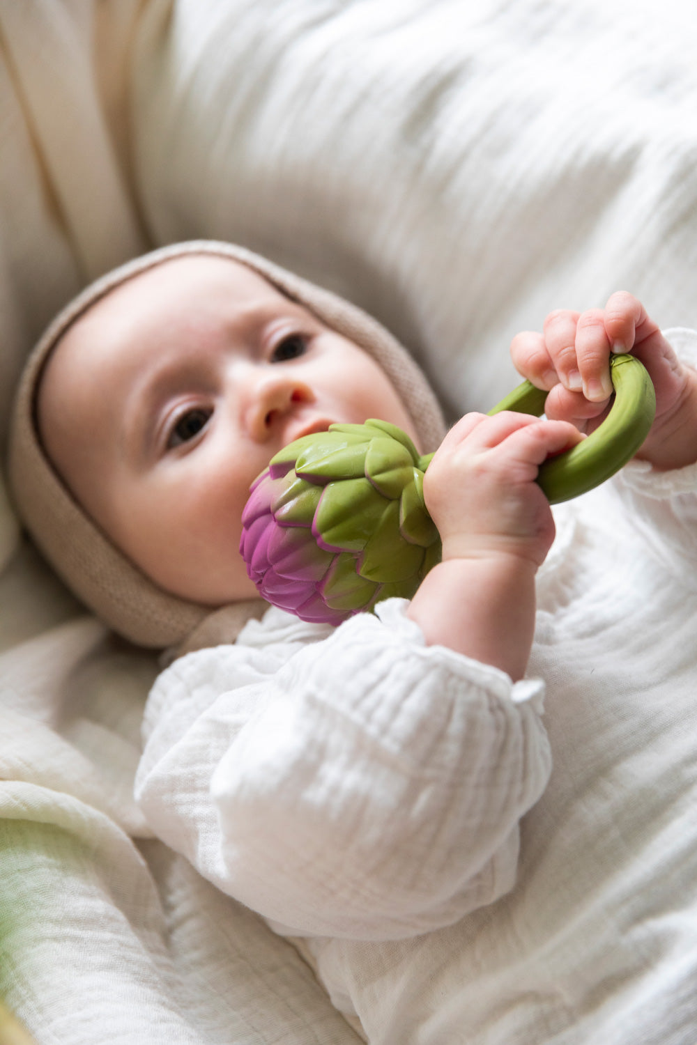 A baby clutching onto an Oli & Carol Artichoke Rattle Teether