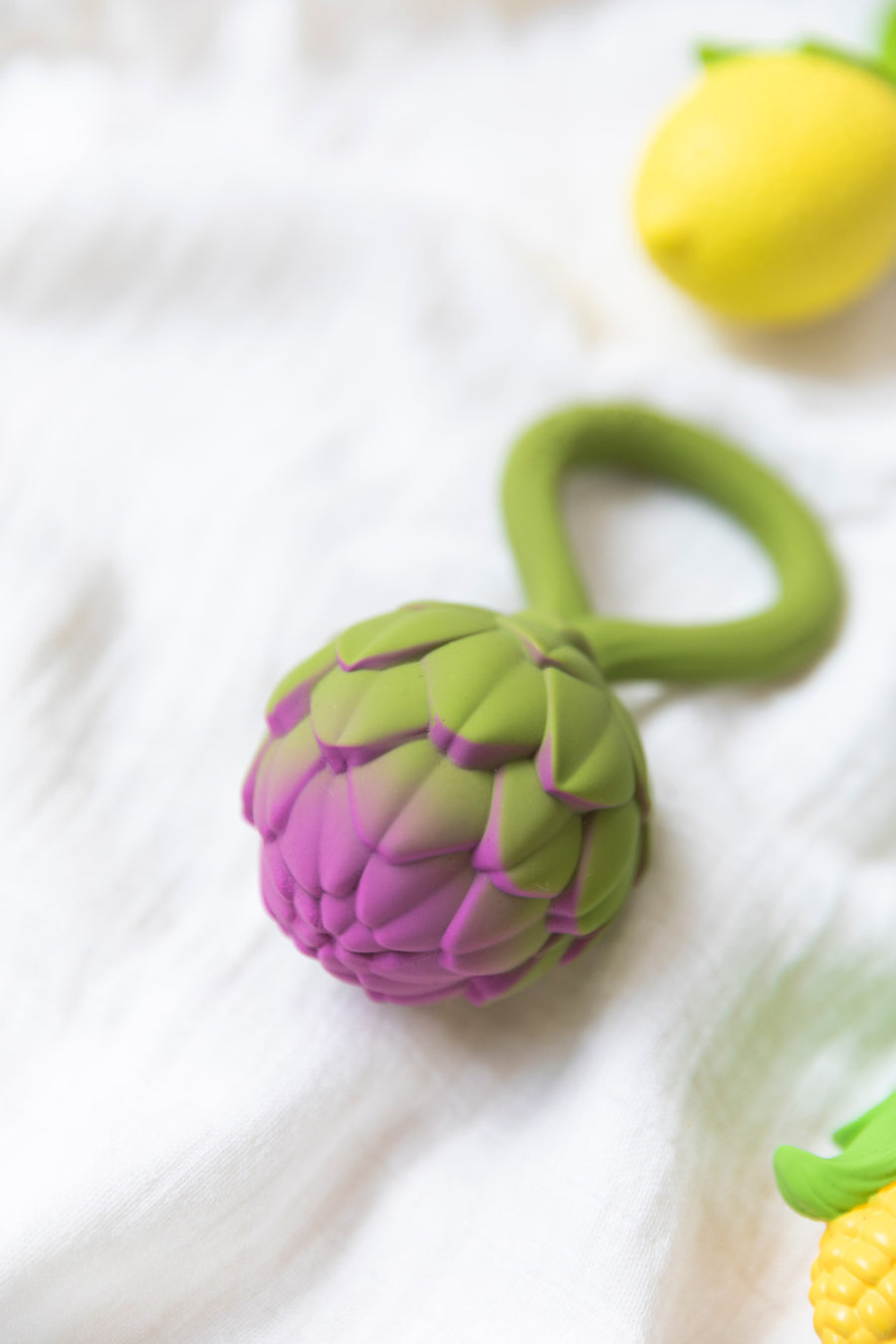 An Oli & Carol Artichoke Rattle Teether placed on white muslin