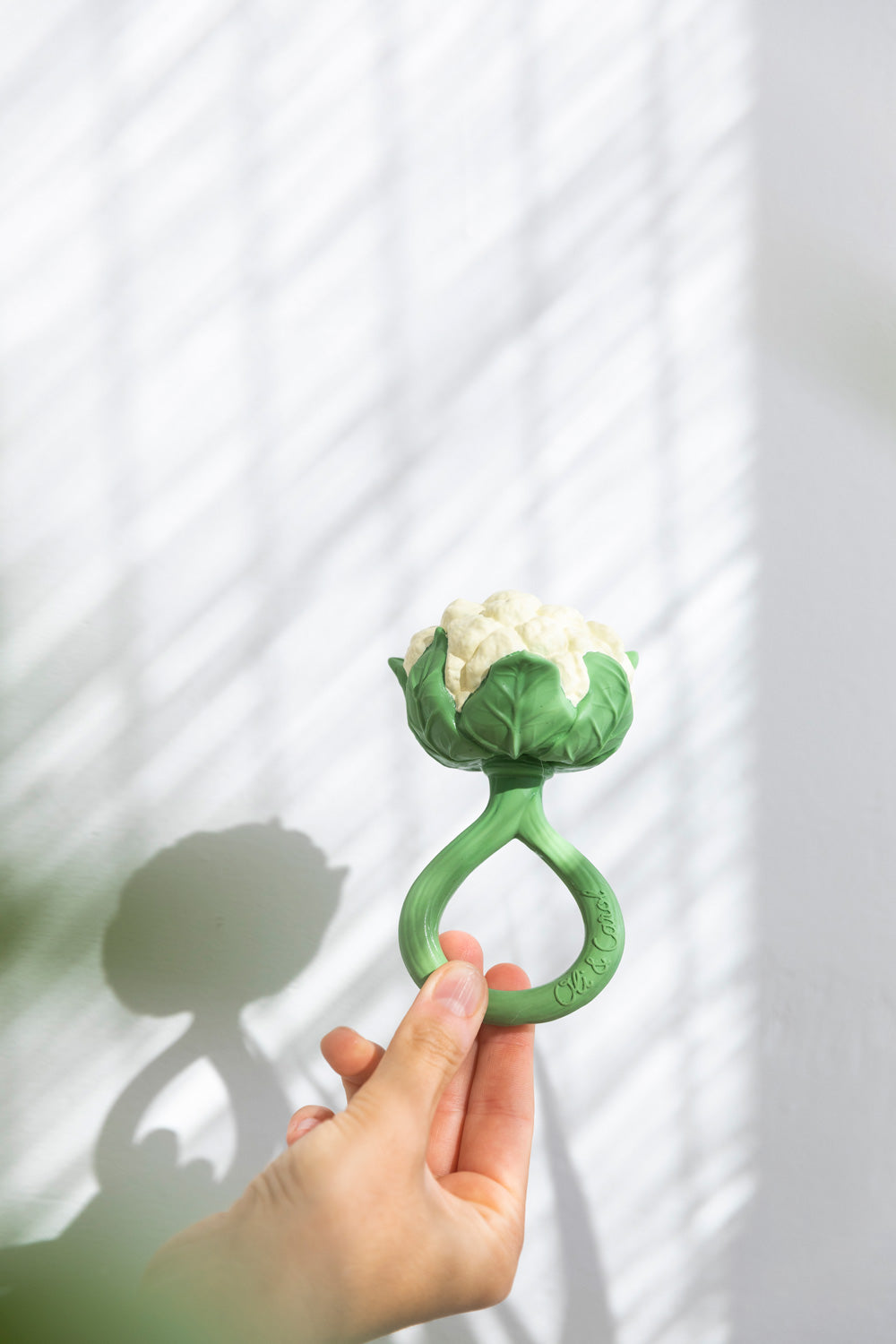 An adult's hand holding up the Oli & Carol Cauliflower Rattle Teether