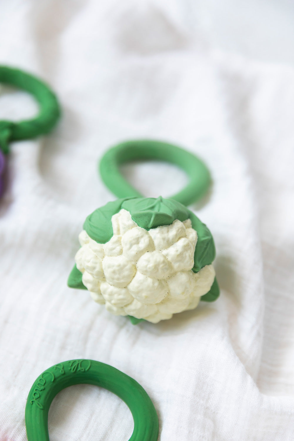 An Oli & Carol Cauliflower Rattle Teether placed an a white muslin