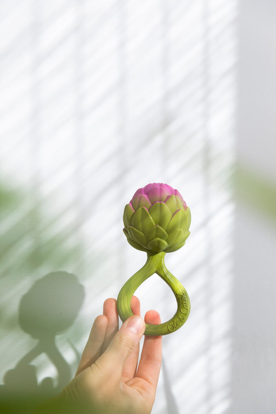 an adult's hand holding up a Oli & Carol Artichoke Rattle Teether