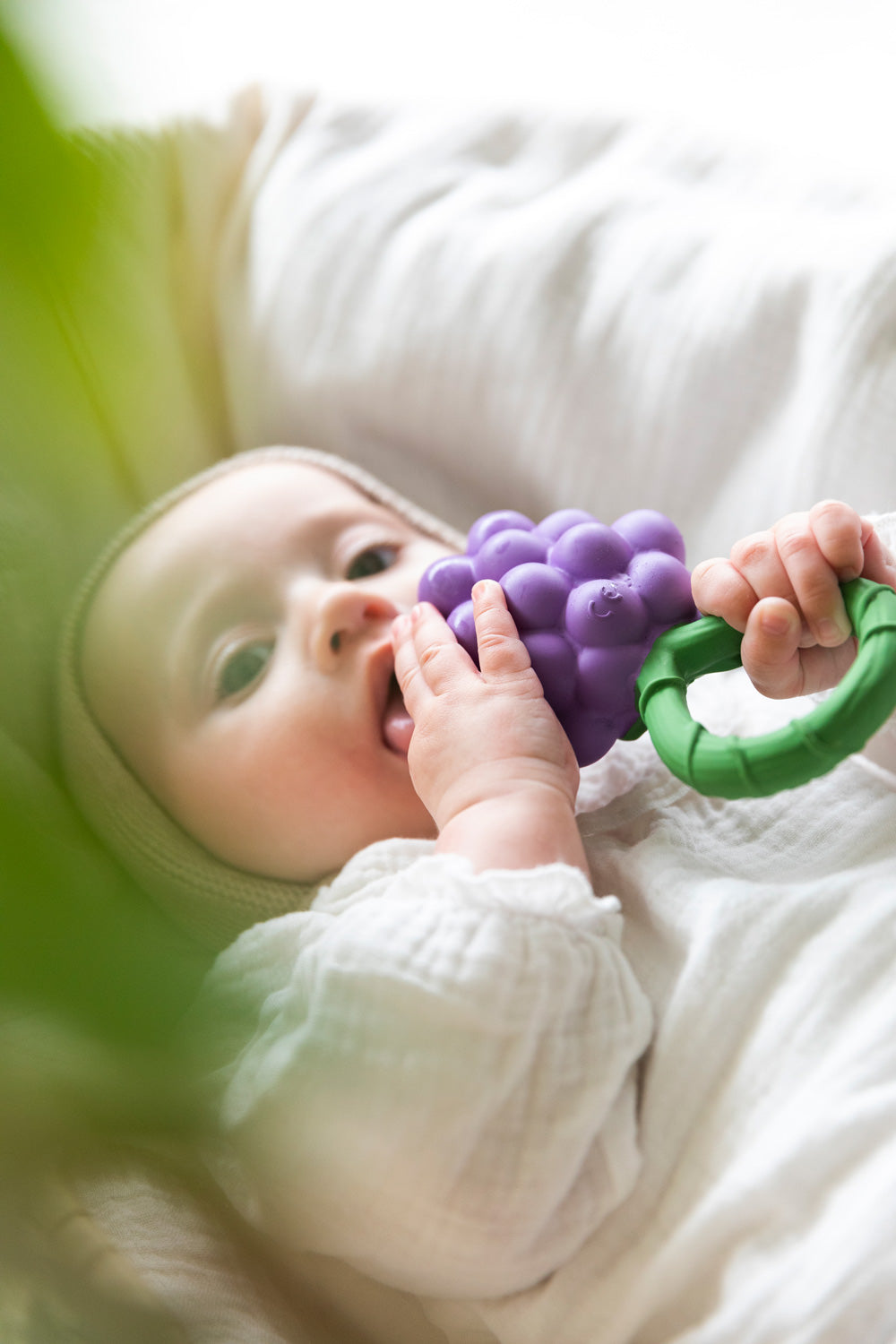 A baby clutching onto Oli & Carol Grape Rattle Teether